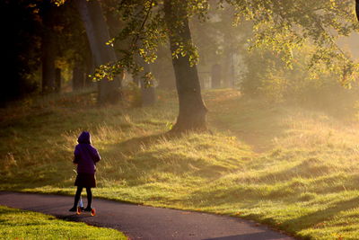 Rear view of girl riding push scooter on footpath