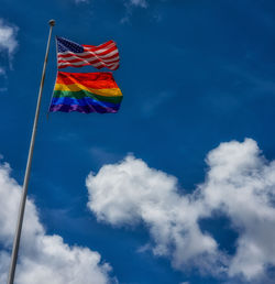 Low angle view of american and rainbow flag against sky