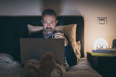 Man works with laptop lying on bed. male home working. boy sitting in bedroom use online devices.