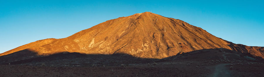 Low angle view of volcanic mountain against blue sky