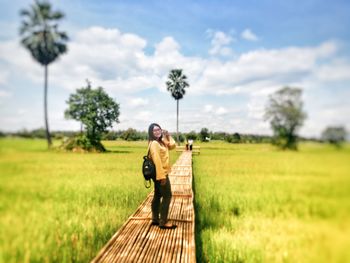 Side view of woman standing on boardwalk at rice paddy against cloudy sky