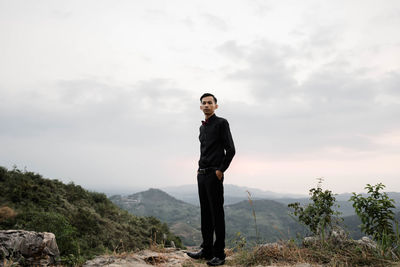 Young man standing on mountain against sky