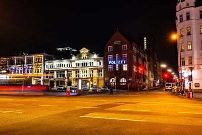 Illuminated city street by buildings at night
