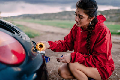 Young woman pouring drink in cup by car