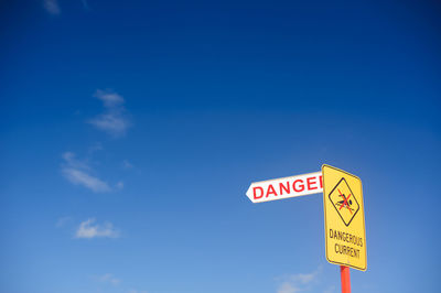 Low angle view of danger sign against sky