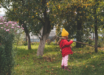 Child in the autumn garden with a rake, girl looking to the side. seasonal backyard work
