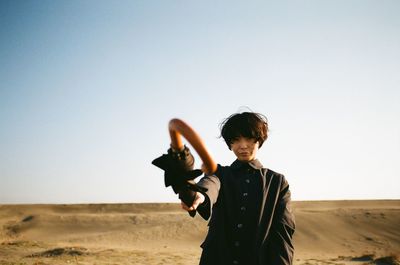 Portrait of woman holding umbrella while standing on sand against clear sky