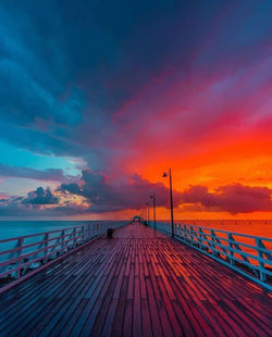 Pier over sea against dramatic sky during sunset