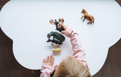 Little girl toddler playing with animal toys on table in children's room at home, view fron top