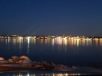 Illuminated city by sea against clear sky at night