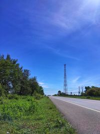 Road by telecommunication tower against blue sky