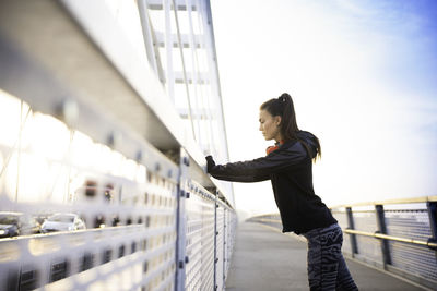 Side view of woman standing on railing against sky