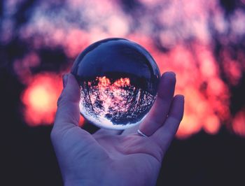 Close-up of hand holding crystal ball against sky