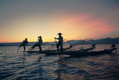 People and fishing nets in boats on sea during sunset