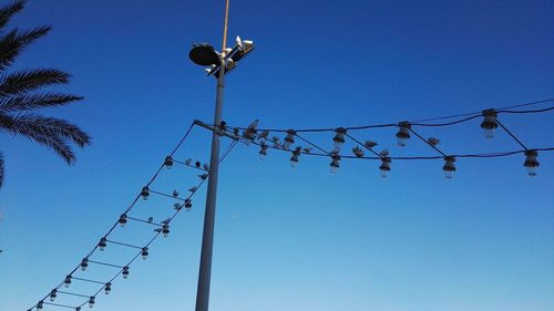 Low angle view of electricity pylon and pigeons against clear blue sky