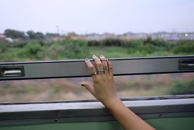 Close-up of hand holding cigarette on railing against sky