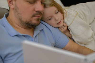 Dad entertains the child during illness, he looks, reads a book, a photo book with his daughter home