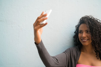 Portrait of smiling young woman using mobile phone against wall