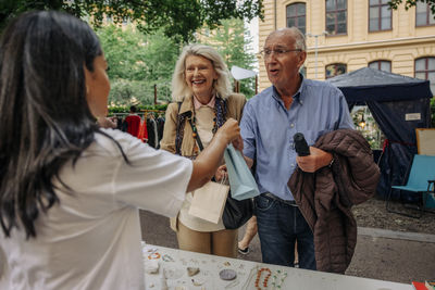 Happy senior couple taking shopping bag from owner at market