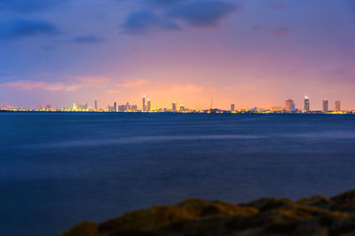 Sea by buildings against sky during sunset