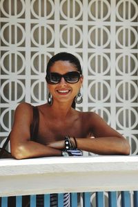 Portrait of smiling young woman wearing sunglasses standing indoors