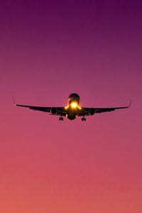 Front silhouette of two jet engine commercial plane landing during sunrise, colorful sky.