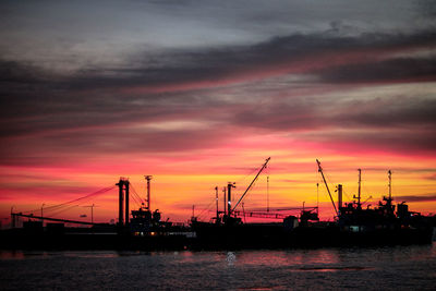 Silhouette cranes at harbor against sky during sunset