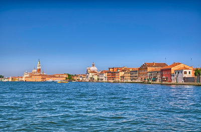 View of buildings at waterfront against blue sky