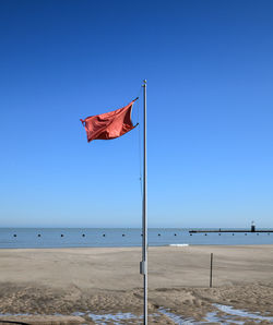Flag on beach against clear blue sky