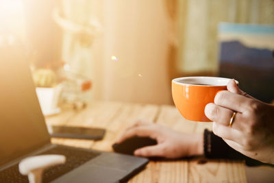 Midsection of man holding coffee cup on table