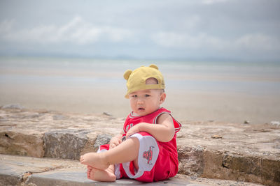 Portrait of boy sitting on shore at beach against sky