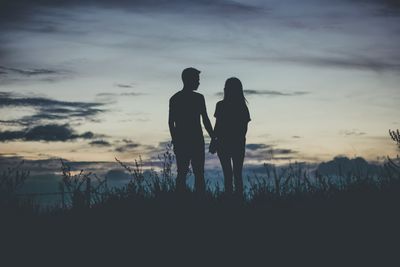 Silhouette men and women standing on field against sky during sunset