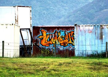 Graffiti on wall by field against sky