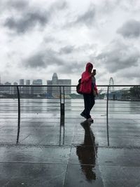 Woman using phone while standing by railing against marina bay financial centre during rainy season