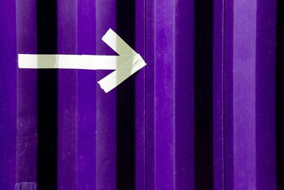 Full frame shot of arrow symbol on purple corrugated iron