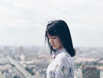 Young woman standing against sky in city