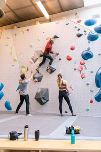 Mature coach showing wall climbing to male and female in gym