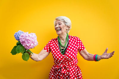 Senior woman holding flower standing against colored background