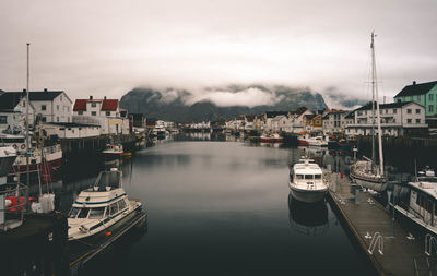 Boats moored at harbor in city against sky