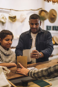 Man paying through smart phone near daughter and saleswoman at checkout in boutique