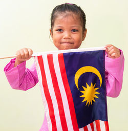 Cute girl holding malaysian flag against wall