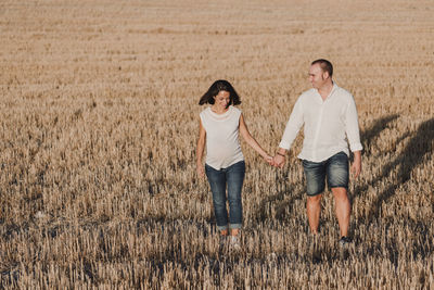 Smiling pregnant woman with man walking on field