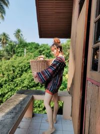 Full length of woman holding basket against tree