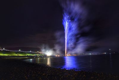 Firework display over river against sky at night