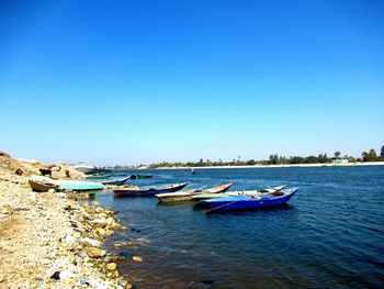 Boats moored in sea against clear blue sky