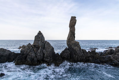 Rocks on shore by sea against sky