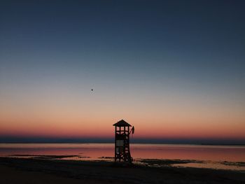 Lifeguard hut on beach against clear sky during sunset