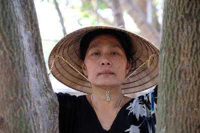 Portrait of mature woman wearing asian style conical hat by tree in forest