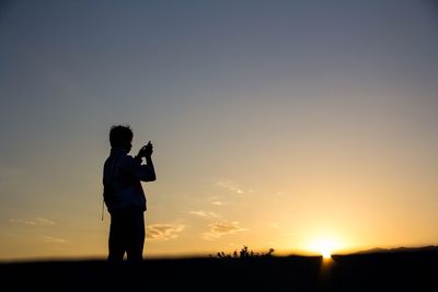 Silhouette man photographing at sunset
