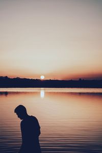 Silhouette man standing on shore against sky during sunset